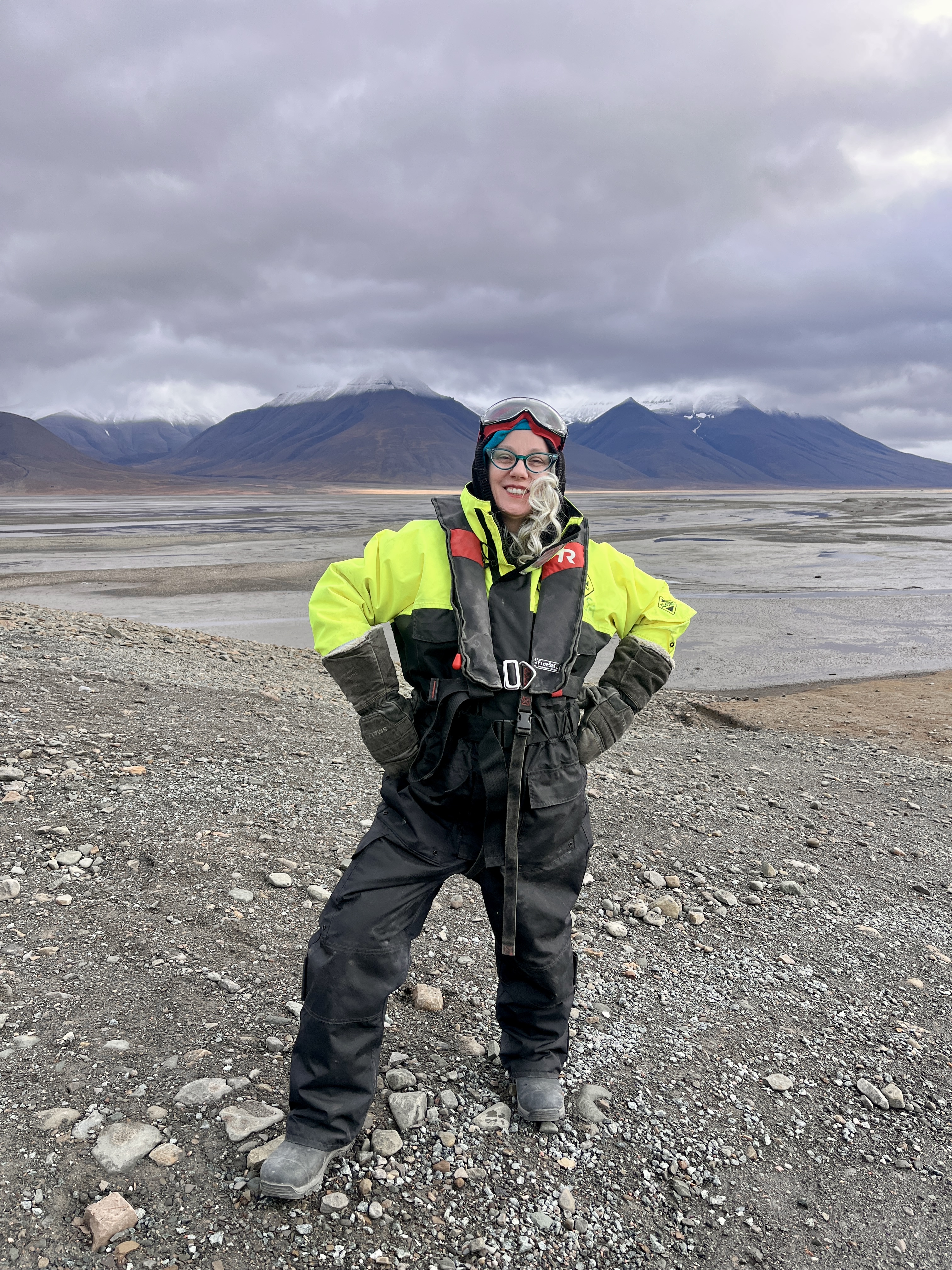 Amy Kitcher smiling in cold-weather expedition gear on a rocky, mountainous landscape